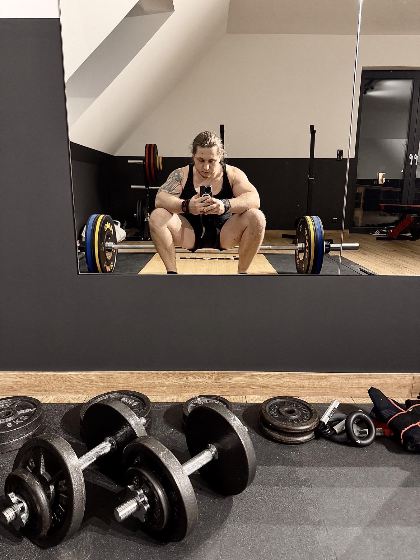 Konrad Dumowski podczas treningu w prywatnym studio, widziany w lustrze na podeście treningowym.